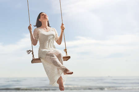 beautiful young woman on a swing on summer day outdoorsの写真素材