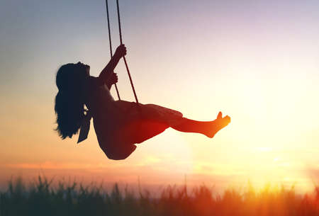 Happy laughing child girl on swing in sunset summerの写真素材
