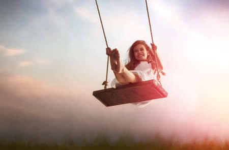 Happy laughing child girl on swing in sunset summerの写真素材