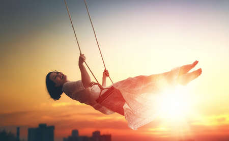beautiful young woman on a swing on summer sunset outdoorsの写真素材
