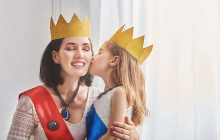 Happy loving family is preparing for a costume party. Mother and her child girl playing together. Beautiful queen and princess in gold crowns.の写真素材