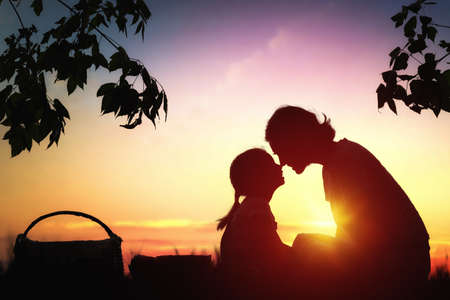 Family picnicking together. Young mother and her child daughter girl enjoying a healthy outdoor meal sitting together on green grass in summer park.の写真素材