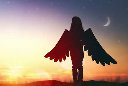 Little girl plays outdoors. Child on the background of sunset sky. Kid with the wings of a bird dreams of flying.の写真素材