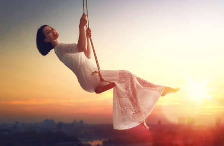 beautiful young woman on a swing on summer sunset outdoorsの写真素材