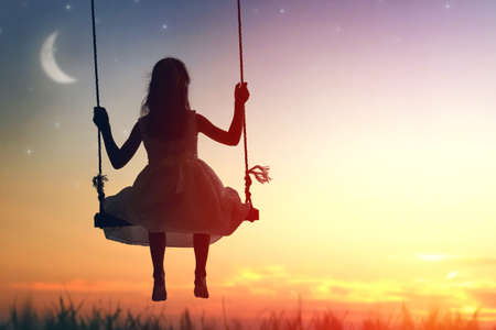 Happy child girl on swing in sunset summerの写真素材