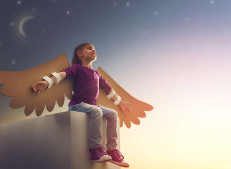 Little girl plays outdoors. Child on the background of sunset sky. Kid with the wings of a bird dreams of flying.の写真素材