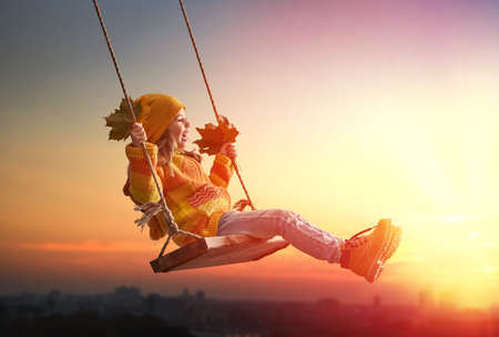 Happy child girl on swing in sunset fall. Little kid playing in the autumn on the nature walk.の写真素材