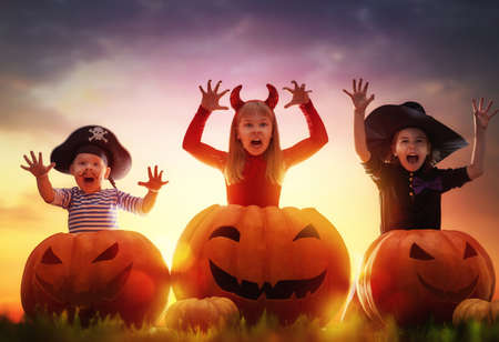 Happy brother and two sisters on Halloween. Funny kids in carnival costumes outdoors. Cheerful...