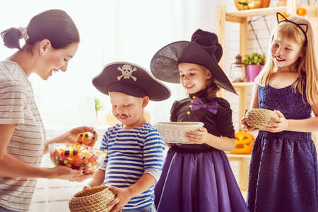 Happy family celebrating Halloween! Young mom treats children with candy. Funny kids in carnival costumes.の写真素材
