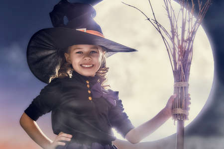 Happy Halloween! Cute little witch with a broomstick. Beautiful young child girl in witch costume...