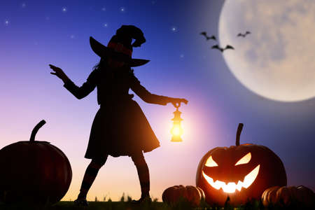 Happy Halloween! Cute little witch with a big pumpkin. Beautiful young child girl in witch costume outdoors.の写真素材