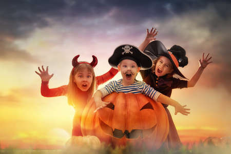 Happy brother and two sisters on Halloween. Funny kids in carnival costumes outdoors. Cheerful children and pumpkins on sunset background.の写真素材
