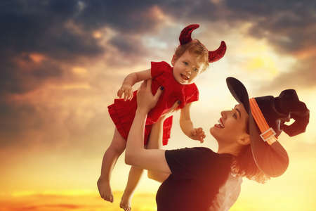 Happy halloween! A mother and her baby daughter in in masquerade dress. Woman in witch costume and baby in devil outfit.の写真素材