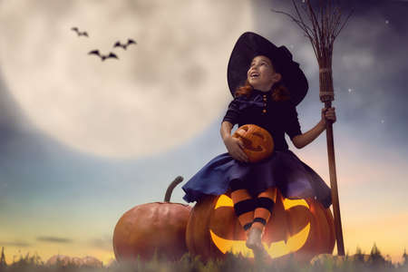 Happy Halloween! Cute little witch with a big pumpkin. Beautiful young child girl in witch costume outdoors.の写真素材