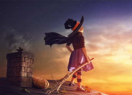 Happy Halloween! Cute little witch with a broomstick. Beautiful young child girl in witch costume on the roof.の写真素材