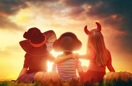 Happy brother and two sisters on Halloween. Funny kids in carnival costumes outdoors. Cheerful children and pumpkins on sunset background.の写真素材