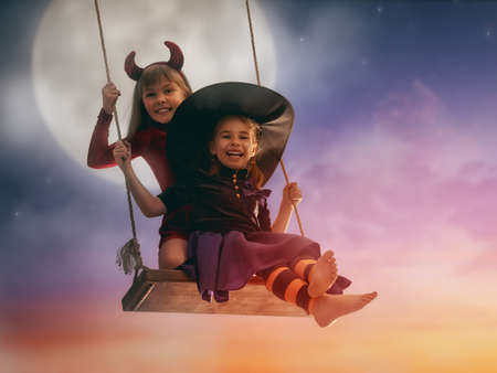 Two happy sisters on Halloween. Funny kids in carnival costumes outdoors. Cheerful children on...