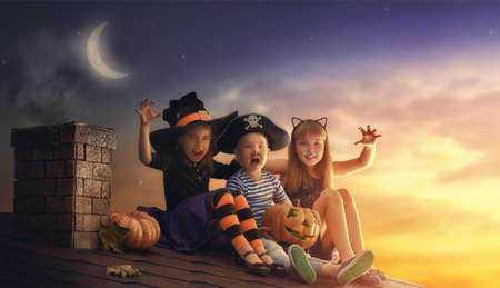 Happy brother and two sisters on Halloween. Funny kids in carnival costumes outdoors. Cheerful children and pumpkins on sunset background.の写真素材
