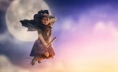 Happy Halloween! Cute little witch flying on a broomstick. Beautiful young child girl in witch...