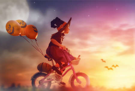 Happy Halloween! Cute little witch with a air ball. Beautiful young child girl in witch costume outdoors.の写真素材