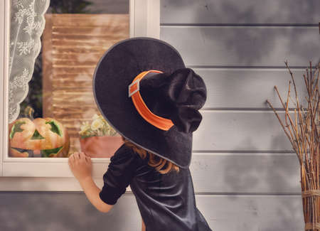 Happy Halloween! Cute cheerful little witch outdoors. Beautiful child girl in witch costume near house decorated to Halloween.の写真素材