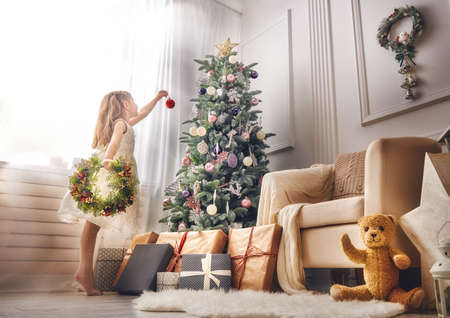 Merry Christmas and Happy Holidays!  Cute little child girl is decorating the Christmas tree indoors.の写真素材
