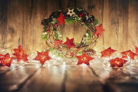 Merry Christmas and Happy Holidays! Red stars, decorative wreath and Christmas garland lights on old dark wooden rustic background.