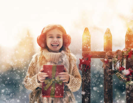 Happy child girl with Christmas gift on a winter walk in natureの写真素材