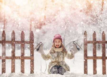 Happy child playing on a winter walk in nature. Cute little kid girl is going skate outdoors.