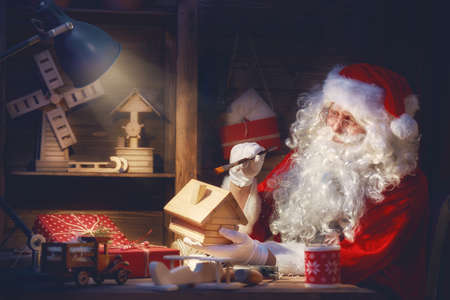 Merry Christmas and Happy Holidays! Santa Clause is preparing gifts for children for Xmas at his desk at home. Christmas legends and traditions.の写真素材
