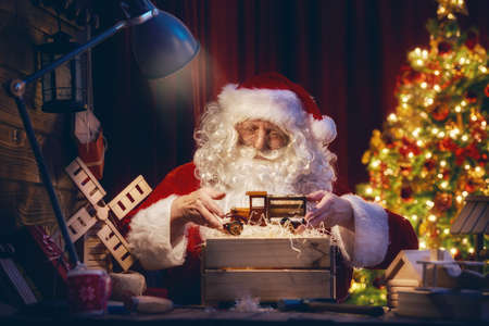 Merry Christmas and Happy Holidays! Santa Clause is preparing gifts for children for Xmas at his desk at home. Christmas legends and traditions.の写真素材
