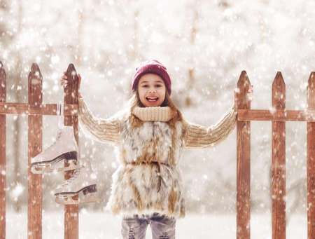 Happy child playing on a winter walk in nature. Cute little kid girl is going skate outdoors.の写真素材