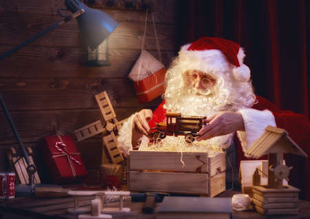 Merry Christmas and Happy Holidays! Santa Claus is preparing gifts for children for Xmas at his desk at home. Christmas legends and traditions.の写真素材