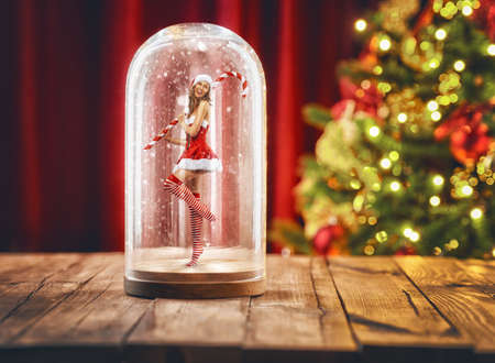 Merry Christmas and happy holidays! Beautiful sexy woman in Santa Claus clothes standing inside glass dome. Santa girl inside a Christmas snow globe.の写真素材