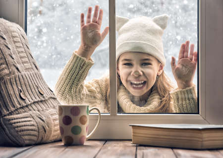 Happy child girl playing on a winter walk in nature. Cute girl looking in window, standing outdoors on winter forest background.の写真素材