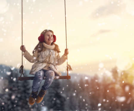Happy child girl on swing in sunset winter. Little kid playing on a winter walk in nature.の写真素材