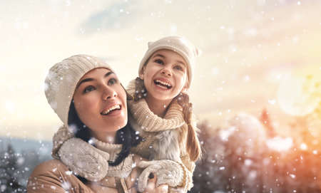 Happy loving family! Mother and child girl having fun, playing and laughing on snowy winter walk in...