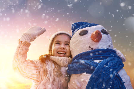 Happy child girl playing with a snowman on snowy winter walk in nature. Frost winter season.の写真素材