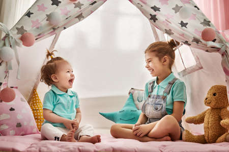 Two cute happy girls play at home. Funny lovely sisters are having fun in children room.の写真素材
