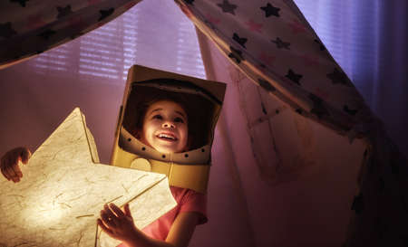 Child in an astronaut costume playing and dreaming of becoming a spacemen. Happy kid plays in tent. Funny lovely girl having fun in children room. の写真素材