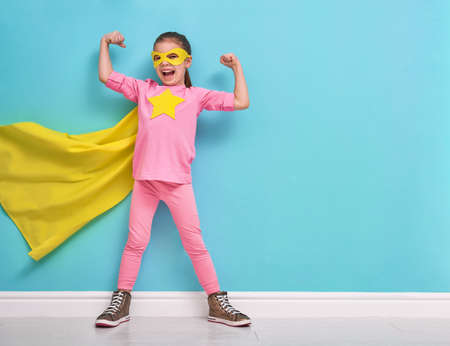 Little child plays superhero. Kid on the background of bright blue wall. Girl power concept. Yellow, pink and  turquoise colors.の写真素材