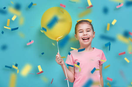 Funny child on a background of bright blue wall. Girl is having fun with balloons and confetti. Yellow, pink and turquoise colors.の写真素材