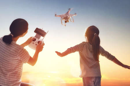Little girl and her mother are operating the drone by remote control in the park. Kid and mom are playing with quadrocopter outdoors. の写真素材