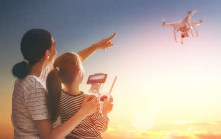 Little girl and her mother are operating the drone by remote control in the park. Kid and mom are playing with quadrocopter outdoors. の写真素材