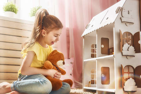 Happy girl plays with doll house and teddy bear at home. Funny lovely child is having fun in kids room.の写真素材