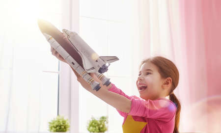 Child girl playing with toy rocket and dreaming of becoming a spacemen. Portrait of funny kid near windows.の写真素材