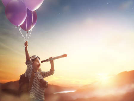 Dreams of travel! Child flying on balloons against the backdrop of a sunset.の写真素材