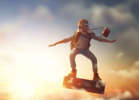 Dreams of travel! Child flying on a suitcase against the backdrop of sunset.の写真素材