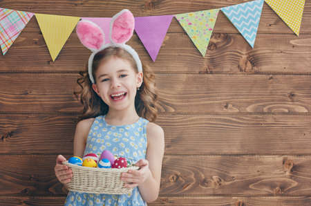 Cute little child wearing bunny ears on Easter day. Girl holding basket with painted eggs.の写真素材