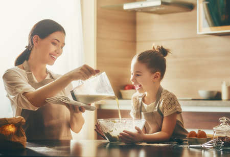 Happy loving family are preparing bakery together. Mother and child daughter girl are cooking cookies and having fun in the kitchen. Homemade food and little helper.の写真素材
